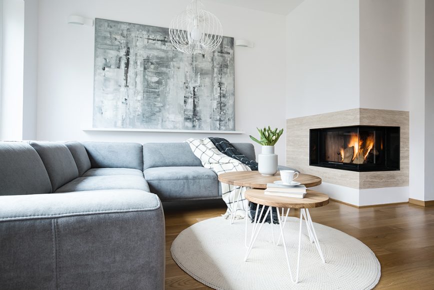 Large L shapped grey sofa in a white room with large corner fireplace