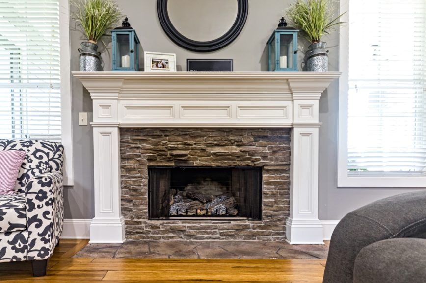 Open fire, stone surround and white mantelpiece with plants, picture frames, candle holders and a mirror