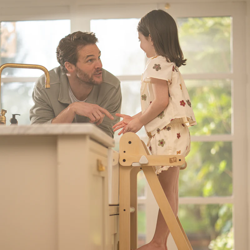 Father and daughter standing by kitchen cupbaord. Girl on step ladder